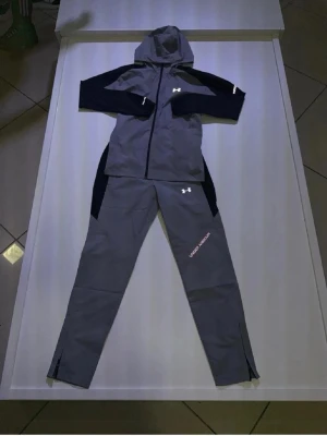 Under Armor Tracksuit - grå/svart - Under armour vindjacka och byxor som matchar. Storlek M men passar även S. Väldigt sällsynt modell. Pris kan diskuteras vid snabb affär!