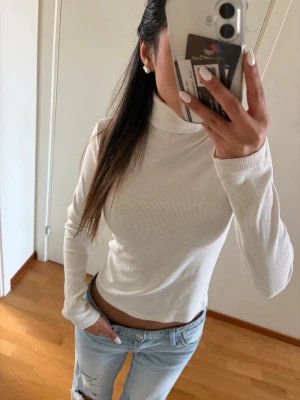 Vit ribbad polotopp - Säljer en vit ribbad polotopp med lång ärm och croppad passform. Toppen är i mjukt material och har en hög krage som ger en clean och stilren look. Perfekt att matcha med jeans eller kjol för en enkel men snygg outfit.En vit polotröja från Zara! I strl M men passar mig som använder S/XS!