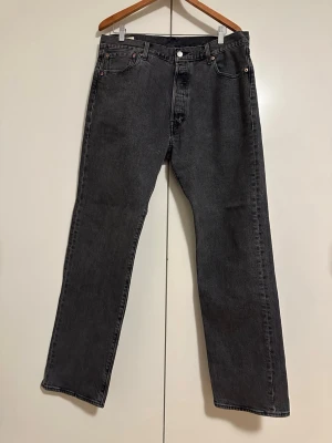 Svarta raka jeans från Levi's - Säljer ett par svarta raka jeans från Levi's med klassisk femficksmodell och knappgylf. Jeansen har en vintagekänsla och är tillverkade i kraftig denim. Passar perfekt till en avslappnad streetwear-look.