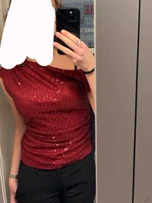 Glittrig vinröd topp med paljetter - Snygg vinröd topp med glittrande paljetter och oneshoulder-design. Perfekt till fest!