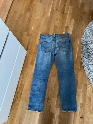 Levi's blå raka jeans - Klassiska blå jeans från Levi's med rak passform och fem fickor. Jeansen har en snygg tvättad look med slitningar och kontrastsömmar. Tillverkade i denim, perfekt för en avslappnad och trendig stil.