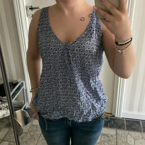 Blåmönstrad topp från Holly & Whyte - Säljer en blå och vit topp från Lindex med småmönstrat tryck i storlek 38. Toppen har v-ringning och är i lätt material, säljer pågrund av att den är inte min stil, OBS LITEN I STORLEKEN