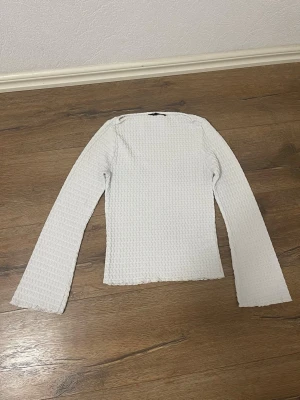 Vit långärmad topp med struktur - Säljer en vit långärmad topp med snyggt strukturerat tyg. Modellen är rak med normal passform och har en enkel, stilren look som passar till det mesta. Perfekt att matcha med jeans eller kjol för en clean vibe. Passar XS också ✨