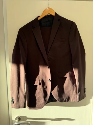 Brun kavaj från Jack & Jones - Snygg brun kavaj från Jack & Jones Premium i super slim fit. Klassisk modell med två knappar framtill, två fickor med lock och en bröstficka. Perfekt för dig som vill ha en stilren och modern look.