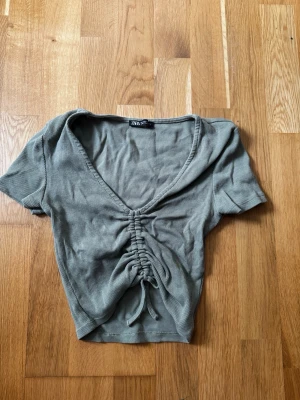Grön ribbad topp från Zara - Trendig grön ribbad topp från Zara med v-ringning och snygg snörning framtill. Kortärmad och croppad modell som passar perfekt till höga jeans eller kjol. Superenkel att styla för en cool vardagslook.