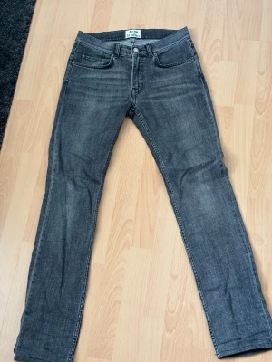 Acne Studios grå jeans - Säljer ett par snygga grå jeans från Acne Studios med klassisk femficksmodell och raka ben. Det står storlek W30/L34 men skulle säga att dom är kortare och passar W30/L32 bättre. Jeansen har en diskret tvättad look och är tillverkade i ett mjukt denimtyg med metallknapp och nitar. Perfekta för en stilren och avslappnad outfit.