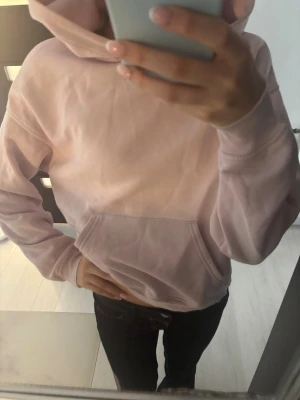 Ljusrosa hoodie gina - Säljer en ljusrosa hoodie med klassisk magficka och huva. Hoodien har ribbade muddar vid ärmsluten och är gjord i mjukt sweatshirtmaterial. Finns några lossade trådar vid luvan (syns på bild) men syns knappt när den är på. Skriv till mig vid frågor och intresse