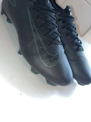 Svarta Nike fotbollsskor med dobbar - Säljer ett par svarta Nike fotbollsskor med klassisk låg profil och snörning. Skorna har en stilren design med diskret Nike-logga på sidan och ovandel i syntetmaterial som ger bra bollkontroll. Perfekta för dig som vill ha grymt grepp på planen. Ända felet är att de saknar sulan men man kan lägga vilken sula som helst 