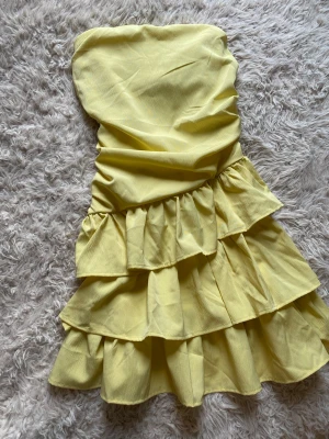 Snygg gul volangklänning - Söt gul axelbandslös klänning med volanger. Köpt från second hand butik och lapparna är avklippta från tidigare ägare. Skulle säga att den är i strl xs/s! 💛 Postar inom 24h📦