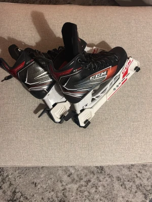 CCM  hockeyskridskor - Säljer ett par svarta och röda CCM  hockeyskridskor med vita detaljer. Skridskorna har snörning, robust kolfiberliknande material och tydlig logga på sidan. Perfekta för dig som vill ha bra stöd och kontroll på isen. Storlek 42