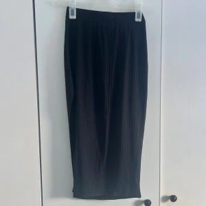 Svart kjol  - Säljer en svart kjol från SHEIN i storlek XS. Kjolen har resår i midjan och är gjord i ett lätt, syntetiskt material som ger ett snyggt fall. Perfekt att styla med både sneakers och boots. Längd: 77cm