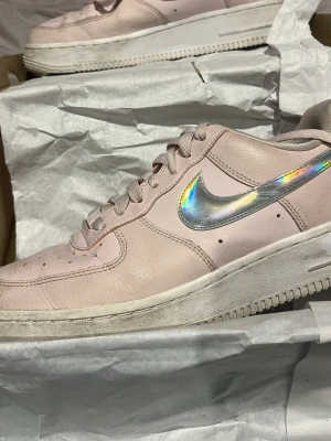 Nike Air Force 1 rosa med holografisk swoosh - Säljer ett par Nike Air Force 1 sneakers i ljusrosa läder med en riktigt snygg holografisk swoosh på sidan. Klassisk låg modell med vit sula och diskret Nike Air-logga bak. Perfekta för dig som vill sticka ut lite extra med dina skor. Skon kosta 500 när jag köpte den. 
