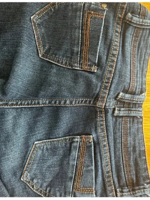 Mörkblå raka jeans - Säljer ett par vintage mörkblå raka jeans  med kontrastsömmar. Jeansen har normalhög midja. Materialet är stretchigt denim för extra komfort. Perfekta till din vardagsstil! Innebenslängden- 73cm hela längden- 93cm
