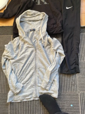 Grå zip hoodie från Polo Ralph Lauren med nike byxor och Calvin Klein hoodie - Snygg grå zip-hoodie från Polo Ralph Lauren med dragsko i huvan och klassisk blå logga broderad på bröstet. Tillverkad i mjukt bomullsmaterial och har två fickor framtill. Perfekt för en chill och avslappnad stil.