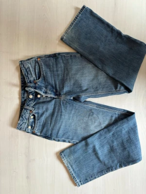 Blå Mid Waist Weekday jeans med raka ben - Säljer ett par klassiska blå Mid Waist Weekday jeans med raka ben och knappgylf. Jeansen har fem fickor och är gjorda i slitstarkt denim. Perfekt för dig som gillar tidlös stil och vill ha ett par jeans som funkar till allt.