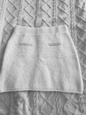 Vit stickad kortkjol från Mango, L - Supersöt vit stickad kortkjol från Mango,  med ribbad midja och två dekorativa fickor fram. Kjolen har en mjuk och mysig känsla, perfekt för att styla med en oversized tröja eller crop top. Storlek L