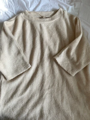 Beige ribbad tröja från Soyaconcept - Säljer en beige ribbad tröja från Soyaconcept med trekvartsärmar och rund hals. Tröjan har en avslappnad passform och är tillverkad i ett mjukt, strukturerat material som känns skönt mot huden. Perfekt för en enkel och stilren look.