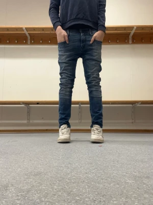Blå slim fit replay jeans herr - Säljer ett par blå slim fit jeans med klassisk femficksdesign och lätt tvättade detaljer. Storlek 29 30. Jeansen har smal passform och normal midja, perfekta till sneakers och hoodie. Materialet är mjukt och stretchigt för extra komfort. De är dock uppsydda men inget som syns.