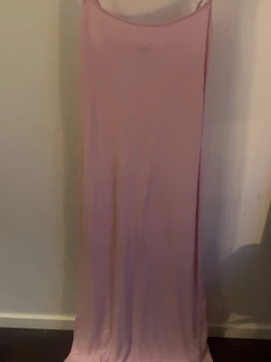 Lång ljusrosa klänning med smala axelband - Enkel och stilren långklänning i ljusrosa med smala axelband. Klänningen har tajt passform  och är ärmlös, perfekt för varma dagar eller när du vill ha en minimalistisk look. Materialet känns mjukt och följsamt mot kroppen.