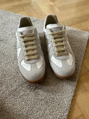 Maison Margiela gats - Snygga sneakers från Maison Margiela i vitt och ljusgrått läder och mocka. Klassisk låg modell med beige snörning och gummisula. bara använt dem en gång. 