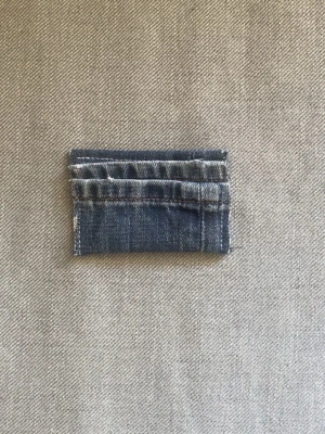 Plånbok i denimtyg - En unik liten plånbok gjord av återvunnen blå denim. Rektangulär form med synliga sömmar och råa kanter för en cool, avslappnad look. Perfekt för kort eller mynt. Plånboken är gjord av vårat uf företag på 5 tjejer som heter deni_mdesign.