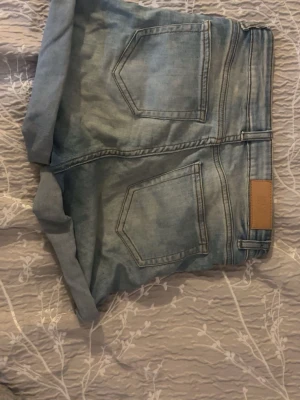 Ljusblå denimshorts med uppvik - Säljer ett par ljusblå denimshorts från Amisu med klassisk femficksmodell och uppvikta benslut. Shortsen har normal passform, bälteshällor och knappgylf. Perfekta för varma dagar och enkla att matcha med olika toppar.Skriv dm för mer bilder!🤍