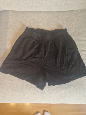 Svarta shorts från H&M i bomull - Svarta shorts från H&M i mjuk bomull med elastisk midja. De har en avslappnad passform och är perfekta för varma dagar. Enkla att matcha med olika toppar och sköna att bära hela sommaren!
