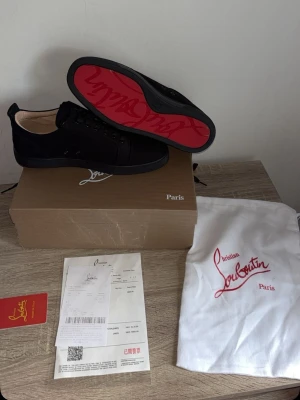 Svarta sneakers från Christian Louboutin - Snygga svarta sneakers från Christian Louboutin med ikonisk röd undersida och diskret logga på sidan. Skorna har klassisk låg profil, svarta skosnören och är tillverkade i ett lyxigt material som känns exklusivt. Perfekt för dig som vill sticka ut med stil. Går med på bytte om man bor k skåne!!