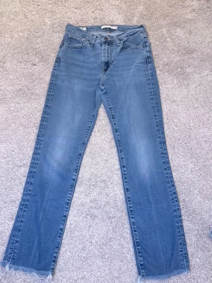 Blå raka jeans med råa kanter - Snygga blå jeans med rak passform och råa, fransiga benslut. Klassisk femficksmodell och normalhög midja. Perfekta för en avslappnad och trendig look. Tillverkade i denim med lätt tvättad effekt.
