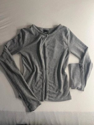 Grå kofta från Gina Tricot - Säljer en enkel och stilren grå kofta från Gina Tricot i storlek XS. Koftan har rund halsringning, långa ärmar och knäppning framtill med små knappar. Materialet är mjukt och tunt, perfekt för lager på lager och en clean look.☺️