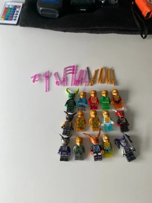 Lego Ninjago minifigurer och vapen - Säljer ett set med 12 olika Lego Ninjago minifigurer i färger som grön, röd, blå, orange och svart. Medföljer flera tillbehör och vapen i rosa och guld plast. Perfekt för dig som gillar att bygga och samla Ninjago-karaktärer.