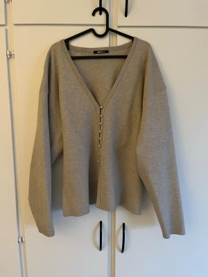 Beige kofta med knappar från Gina Tricot - Beige kofta med djup V-ringning och knäppning framtill. Koftan har långa ärmar och en avslappnad passform. Tillverkad i mjukt material. Perfekt att slänga på sig över en t-shirt eller linne. Katt finns i hemmet