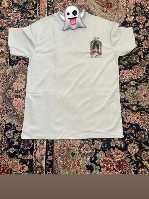 Vit Casa Blanca t-shirt med tryck - Vit t-shirt från Casa Blanca med stort färgglatt tryck av en byggnad och palmer på ryggen samt mindre tryck på bröstet. Klassisk passform och rund halsringning. Perfekt för dig som gillar streetwear och snygga prints.Samma dag du köper samma dag jag fraktar 