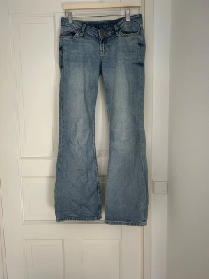 Ljusblå bootcut jeans - Säljer ett par ljusblå bootcut jeans med klassisk femficksdesign och låg midja. Jeansen har en lätt tvättad look och vida ben nedtill. Perfekta för en avslappnad och trendig stil. Dom är från Weekday 