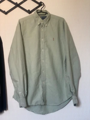 Ljusgrön skjorta från Ralph Lauren - Snygg ljusgrön skjorta från Ralph Lauren med klassisk button-down krage och broderad logga på bröstet. Skjortan har långa ärmar, knäppning framtill och är tillverkad i bomull. Perfekt för en stilren och avslappnad look.