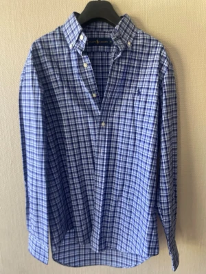 Blårutig skjorta från Ralph Lauren - Klassisk blårutig flanell skjorta från Ralph Lauren. Skjortan har långa ärmar och knäppning framtill. Perfekt för en stilren och avslappnad look.