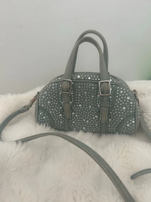 Zara väska - Cool blå handväska i jeansmaterial med massor av nitar. Väskan har både handtag och en avtagbar axelrem, perfekt för att bära på olika sätt. Fint skick förutom att flärpen på dragkedjan är av (bild 3), men går fortfarande att använda som vanligt. Sen har spännena till remen fått en liten färgförändring men inget man direkt tänker på. Köpt här på plick för 450. Mitt pris 350. Kan tänka mig att diskutera priset något vid snabb affär!!