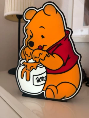 Winnie the Pooh LED-lampa - Säljer en LED-lampa i form av Nalle Puh som doppar händerna i en honungsburk. Lampan är gjord i plast och har starka färger: gul, röd, svart och vit. Perfekt som dekoration i barnrum eller för dig som gillar Disney och tecknade figurer.