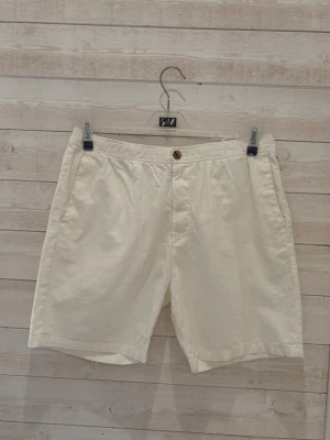 Vita bomullsshorts med knapp - Stilrena vita shorts i bomull med klassisk passform. De har en midwaist design, sidofickor och stängs med en knapp framtill. Perfekta för varma sommardagar och enkla att matcha med olika toppar.