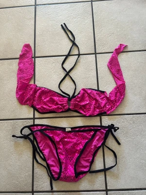 Rosa bikini med svarta detaljer - Snygg rosa bikini från North Blue med svarta kanter och knytband. Både överdel och underdel har glittriga paljetter och prickigt mönster. Perfekt för stranden eller poolen, med trendig look och bekväm passform.
