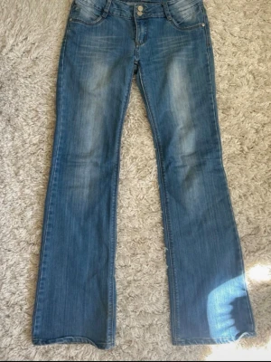 Blå bootcut jeans från Riever - Snygga blå lågmidjade bootcut jeans från Riever med klassisk femficksdesign och dubbla knappar i midjan. Perfekta för en avslappnad och trendig look. Står i dem att de är storlek w 31 vilket ungefär är M men de sitter lite tajtare. Köpt vintage