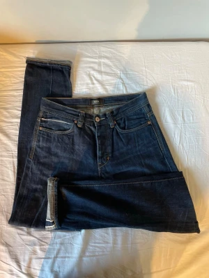 Mörkblå selvedge jeans - Snygga mörkblå jeans från Neuw med klassisk femficksdesign och raka ben. Jeansen har kontrastsömmar och en knappgylf. Perfekta för dig som gillar stilrena och tidlösa denimplagg.