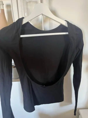 Svart långärmad topp med öppen rygg - Svart långärmad topp med en djup, öppen rygg. Snygg och enkel design som passar perfekt till jeans eller kjol. Tillverkad i ett stretchigt material som sitter tight mot kroppen.