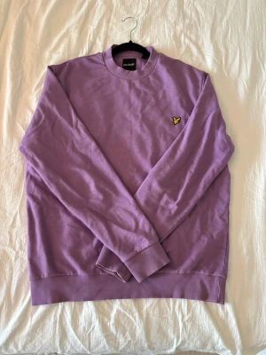 Lila sweatshirt från Lyle & Scott - Säljer en lila sweatshirt från Lyle & Scott med klassisk rund halsringning och ribbade muddar. Tröjan har den ikoniska gula örnloggan på bröstet och är tillverkad i mjuk bomull. Perfekt för en avslappnad och stilren look.