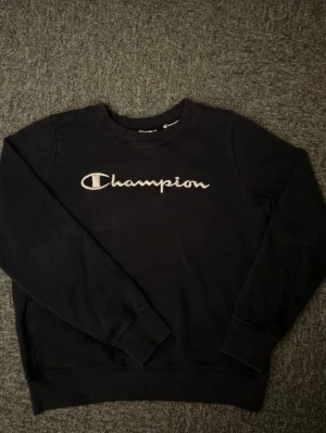 Svart Champion sweatshirt  - Svart sweatshirt från Champion med broderad logga framtill. Klassisk rund halsringning och ribbade muddar vid ärmslut och nederkant.