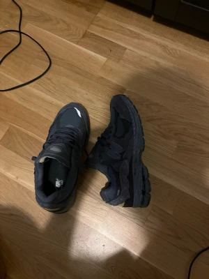 Svarta New Balance sneakers - Snygga svarta New Balance sneakers med mesh och mockadetaljer. Skorna har en chunky sula och klassisk N-logga på sidan. Perfekta för dig som gillar streetwear och vill ha en stilren look med sportig känsla.