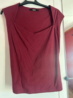 Vinröd topp från BikBok - Snygg vinröd topp från BikBok med v-ringad hals och ärmlös design. Toppen har en enkel och stilren look som passar perfekt till jeans eller kjol💗