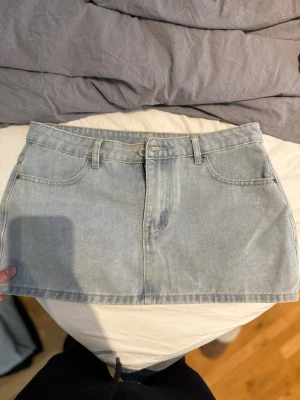 Ljusblå jeanskjol i minilängd - Trendig ljusblå jeanskjol i minilängd med klassisk femficksdesign och bälteshällor. Kjolen har dragkedja och knapp framtill och är tillverkad i denim. Perfekt för en avslappnad och cool stil. Står ingen storlek inuti men är storlek M