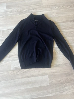 Mörkblå tröja med knappar från Zara - Snygg mörkblå långärmad tröja från Zara med tre knappar vid halsen. Tröjan har en klassisk passform och är tillverkad i mjukt material som känns skönt mot huden. Perfekt för en stilren och enkel look.
