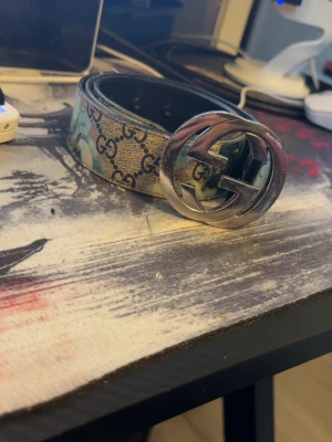 Gucci GG Supreme bälte med silverdetalj - Snyggt Gucci GG Supreme bälte med klassiskt monogrammönster i beige och blå toner samt stor silverfärgad GG-logga som spänne. Bältet är gjort i skinn och har en exklusiv känsla som lyfter vilken outfit som helst. Äkta! Köpt i triangeln på second place i malmö